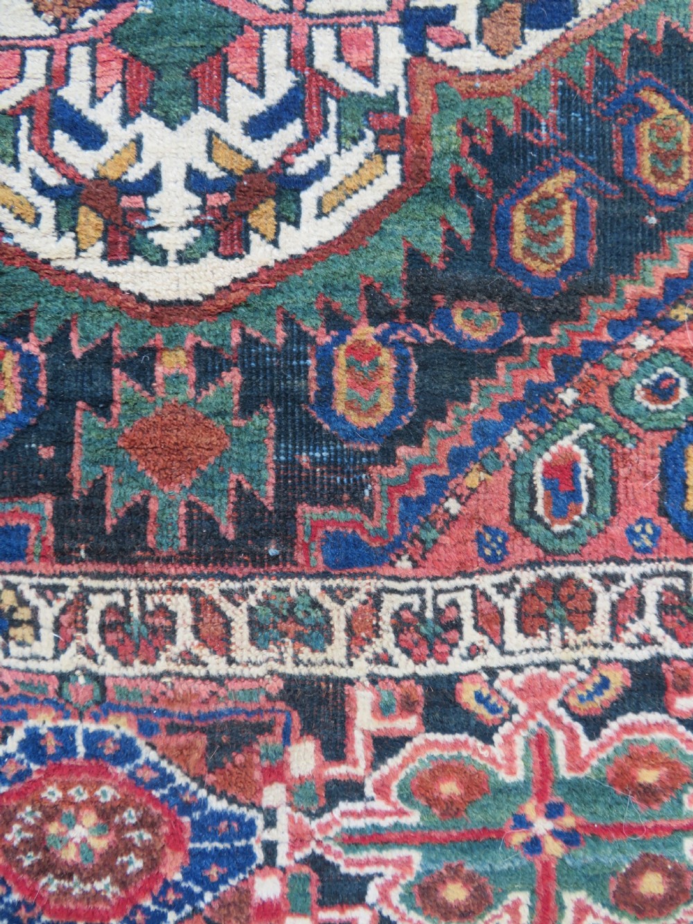 A hand-knotted Bakhtiari tribal wool rug with central ivory and blue medallions framed by a dark navy field with repeating boteh patterns and a detailed geometric border. View VI