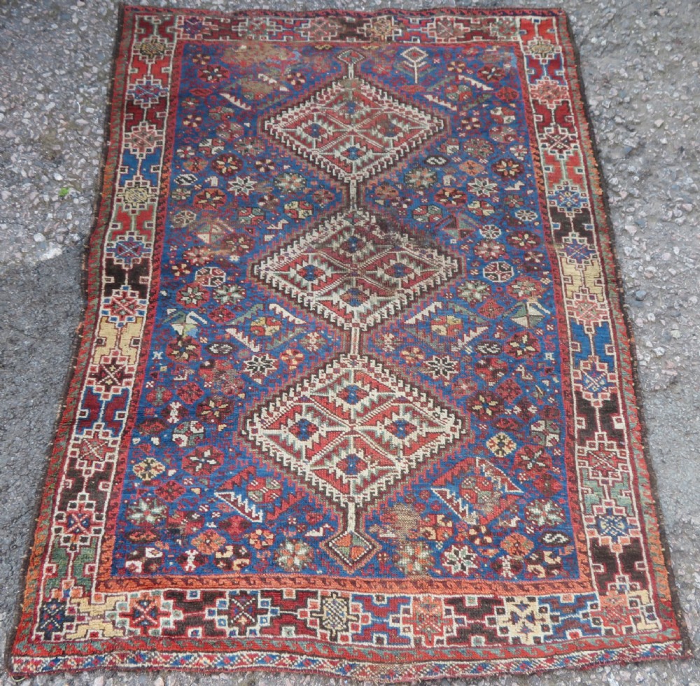 An antique Khamseh hand-knotted wool rug featuring three stacked geometric diamond medallions on an indigo blue field surrounded by intricate patterned borders.