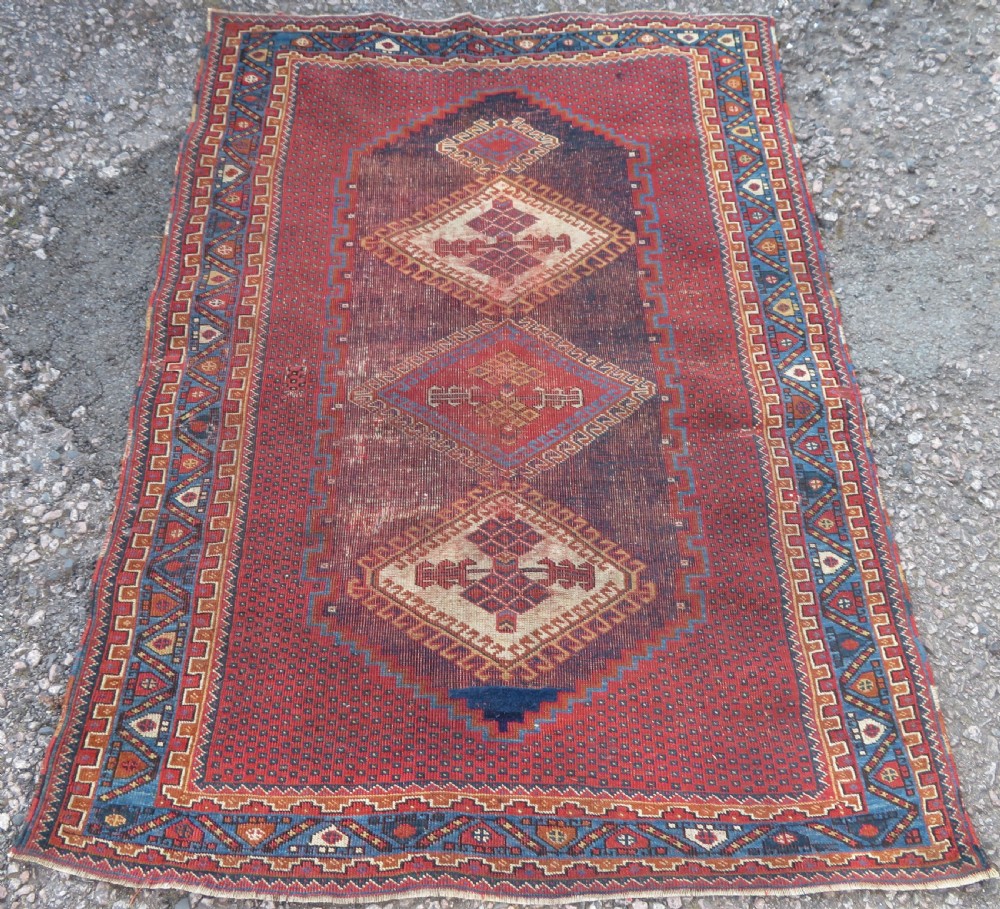 A rectangular hand-knotted wool rug featuring three diamond medallions on a dark central field surrounded by a patterned terracotta red background and geometric borders.