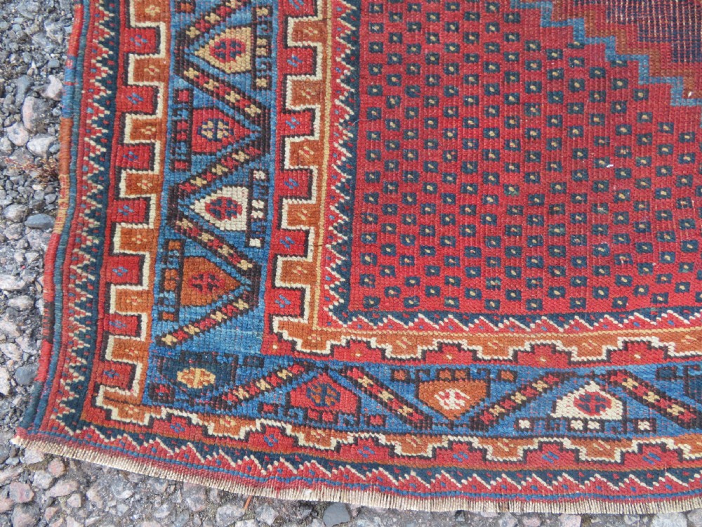 A rectangular hand-knotted wool rug featuring three diamond medallions on a dark central field surrounded by a patterned terracotta red background and geometric borders. View VIII