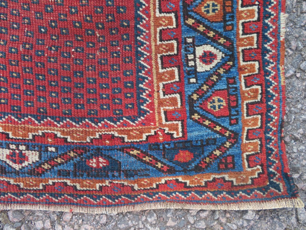 A rectangular hand-knotted wool rug featuring three diamond medallions on a dark central field surrounded by a patterned terracotta red background and geometric borders. View IX
