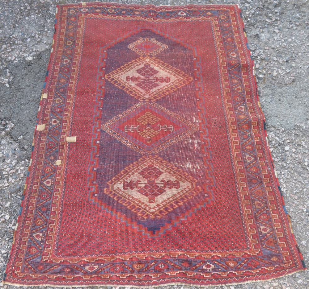 A rectangular hand-knotted wool rug featuring three diamond medallions on a dark central field surrounded by a patterned terracotta red background and geometric borders. View XI