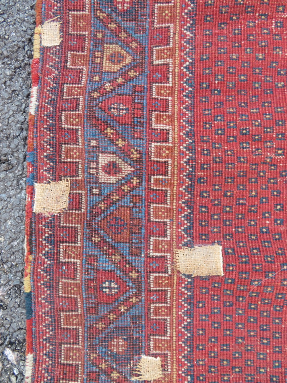 A rectangular hand-knotted wool rug featuring three diamond medallions on a dark central field surrounded by a patterned terracotta red background and geometric borders. View XII