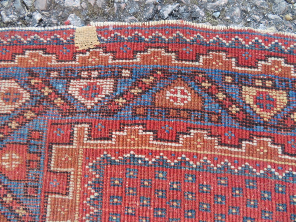 A rectangular hand-knotted wool rug featuring three diamond medallions on a dark central field surrounded by a patterned terracotta red background and geometric borders. View XIII