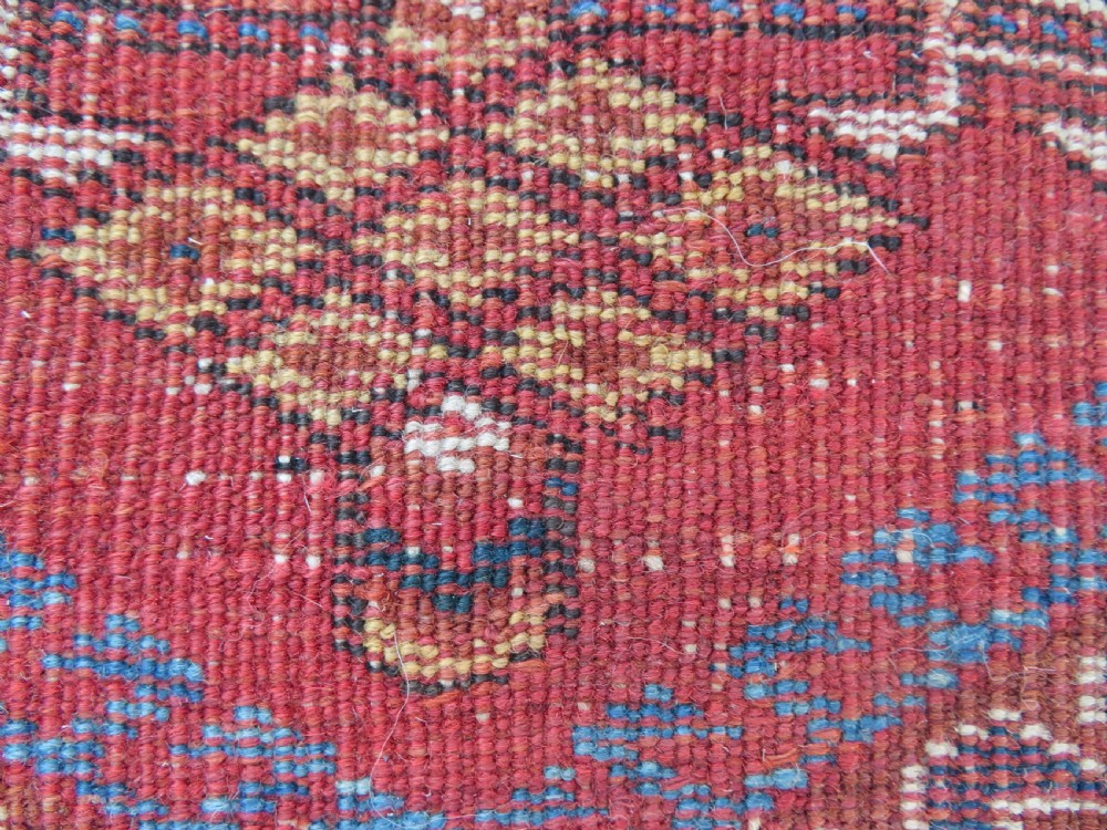 A rectangular hand-knotted wool rug featuring three diamond medallions on a dark central field surrounded by a patterned terracotta red background and geometric borders. View XIV