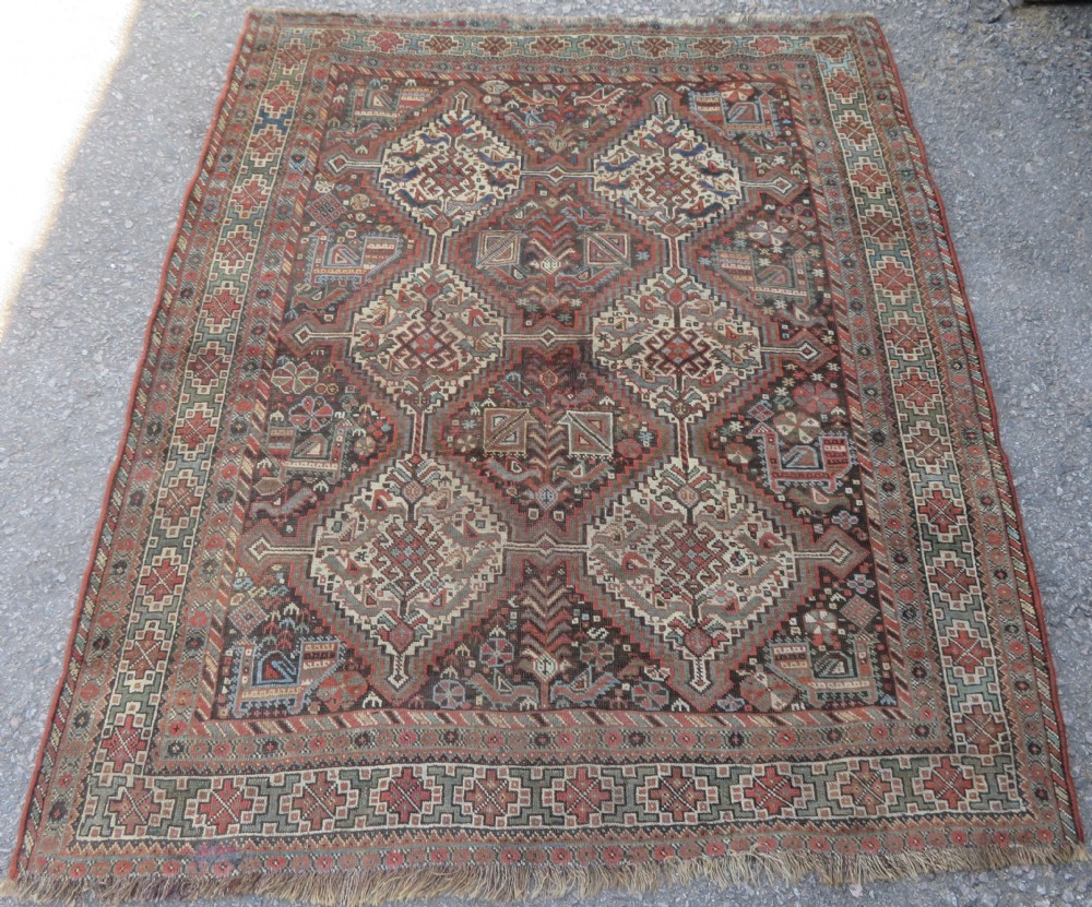 A rectangular hand-knotted antique Khamseh wool rug featuring geometric diamond medallions and intricate border patterns in terracotta, dark brown, and cream.