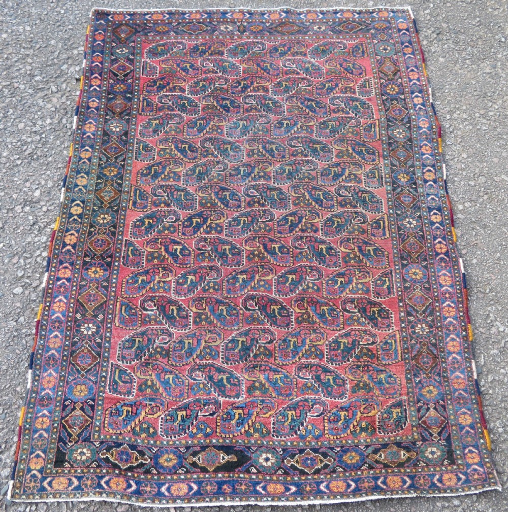 An antique hand-knotted wool Afshar tribal rug featuring a repeating boteh pattern on a terracotta field with geometric blue and cream borders.