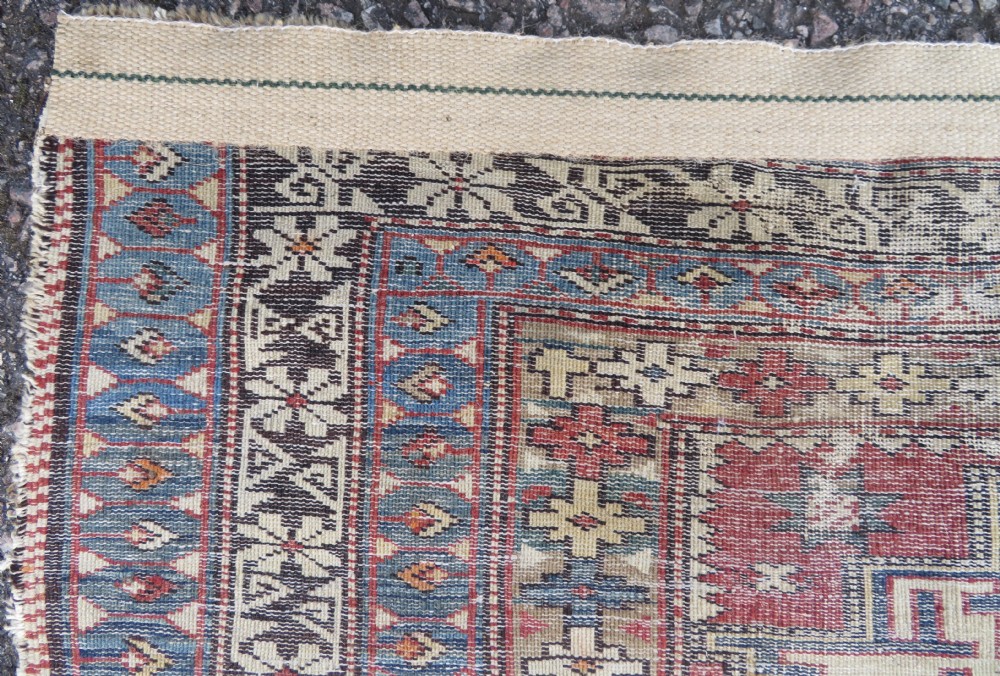 A distressed antique hand-knotted Caucasian Daghestan wool rug featuring geometric medallions and intricate borders in terracotta red, cream, and indigo blue. View XI