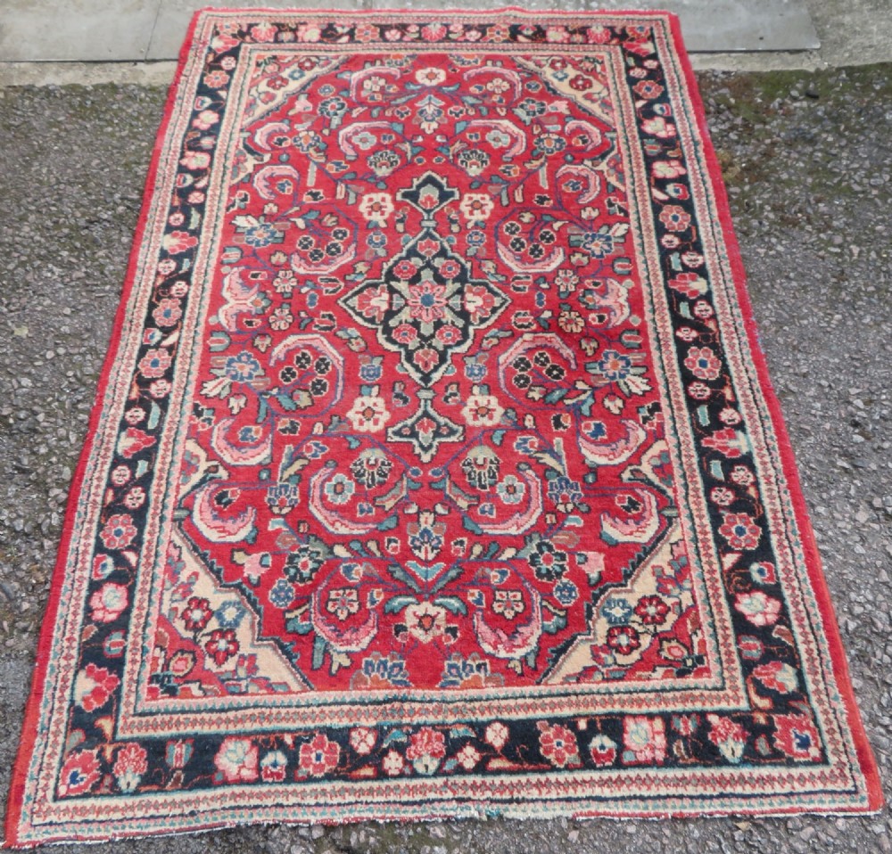 An antique West Persian Mahal rug featuring a red ground, central navy medallion, floral spandrels, and a decorative border.