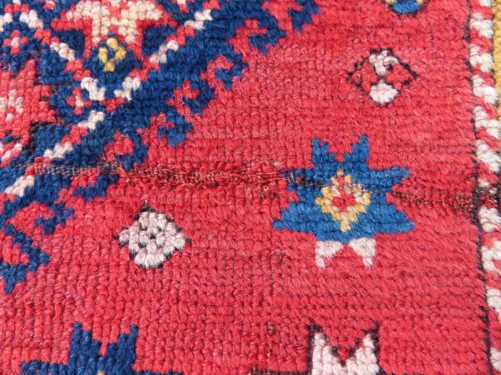 An antique hand-knotted wool rug featuring geometric diamond medallions in red, dark blue, yellow, and cream with a detailed border pattern. View V