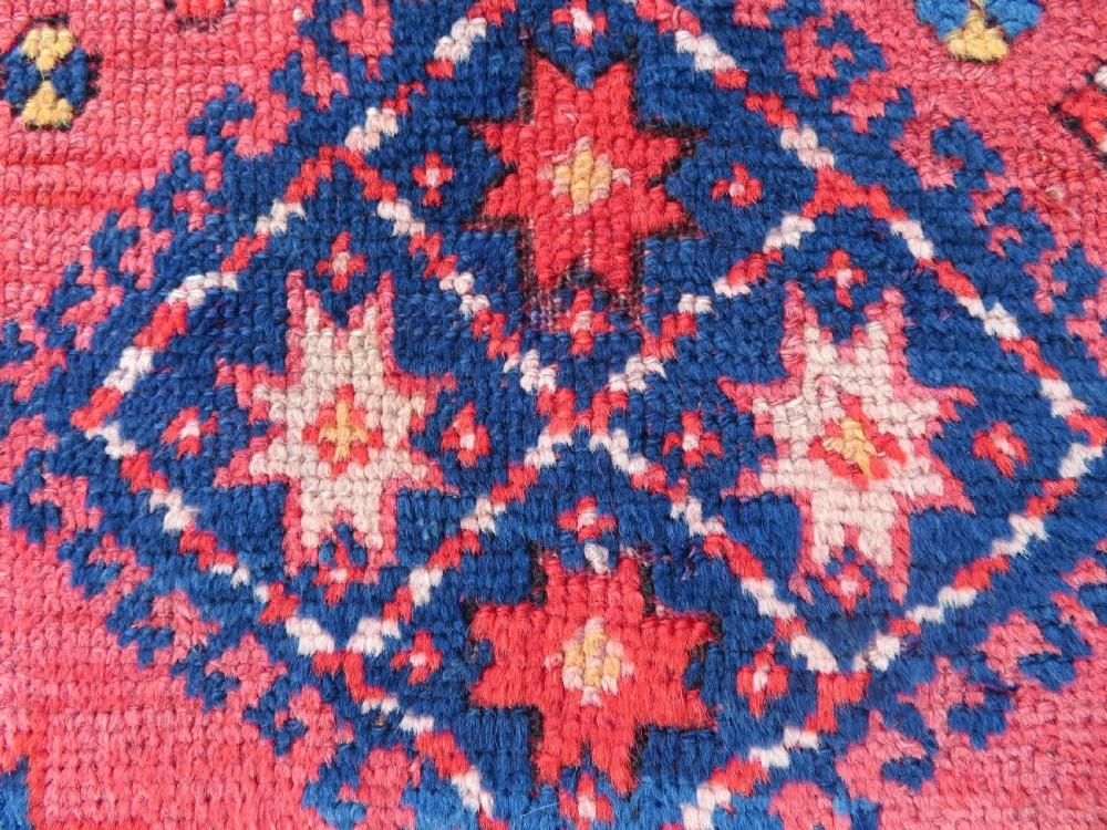 An antique hand-knotted wool rug featuring geometric diamond medallions in red, dark blue, yellow, and cream with a detailed border pattern. View IX