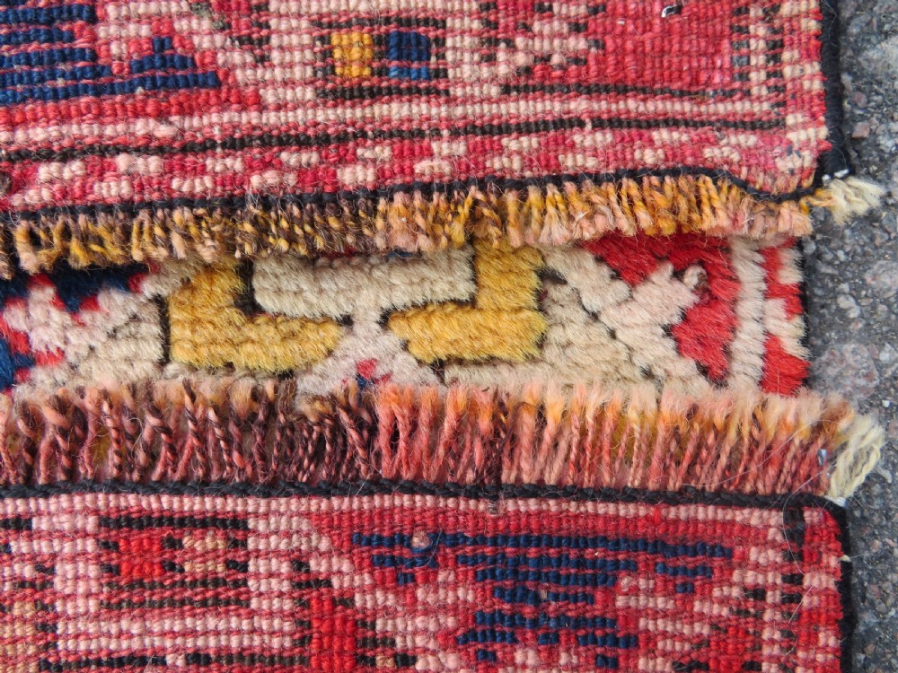 An antique hand-knotted wool rug featuring geometric diamond medallions in red, dark blue, yellow, and cream with a detailed border pattern. View XII