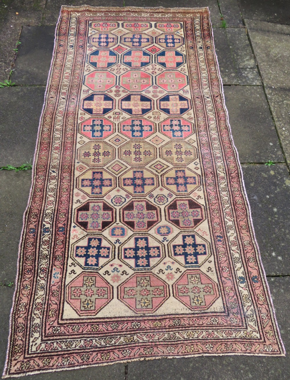 An antique hand-knotted Kurdish runner rug featuring repeating octagonal geometric medallions in pink, indigo, and cream tones.