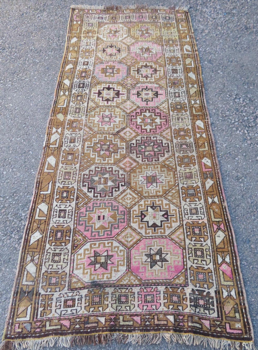An antique Kurdish hand-knotted wool rug runner featuring repeated geometric octagonal medallions in shades of pink, tan, cream, and dark brown.