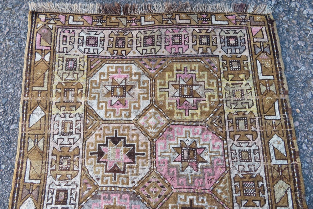An antique Kurdish hand-knotted wool rug runner featuring repeated geometric octagonal medallions in shades of pink, tan, cream, and dark brown. View III