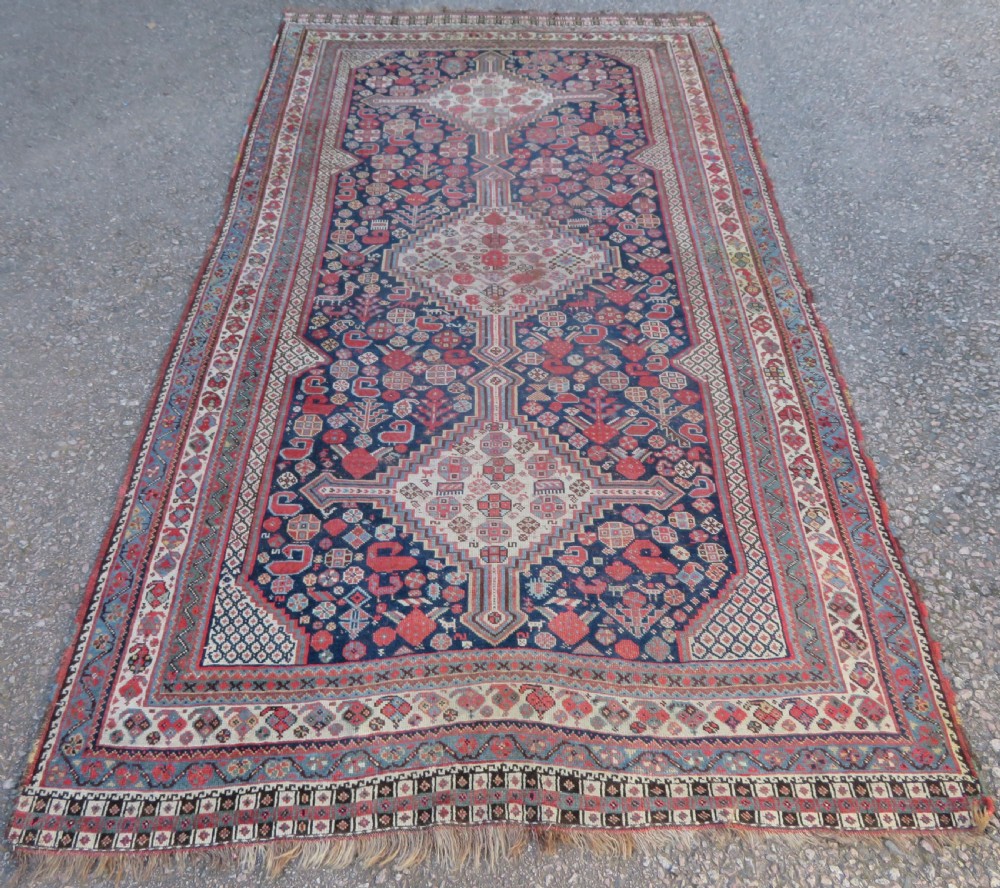 An antique hand-knotted Persian Khamseh carpet featuring three central diamond pole medallions on a dark navy blue field filled with geometric tribal bird and flower motifs surrounded by intricate decorative borders.