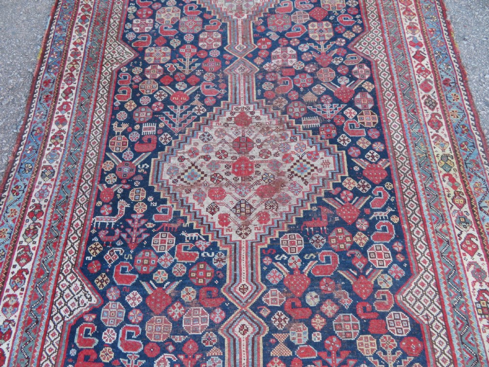 An antique hand-knotted Persian Khamseh carpet featuring three central diamond pole medallions on a dark navy blue field filled with geometric tribal bird and flower motifs surrounded by intricate decorative borders. View IV