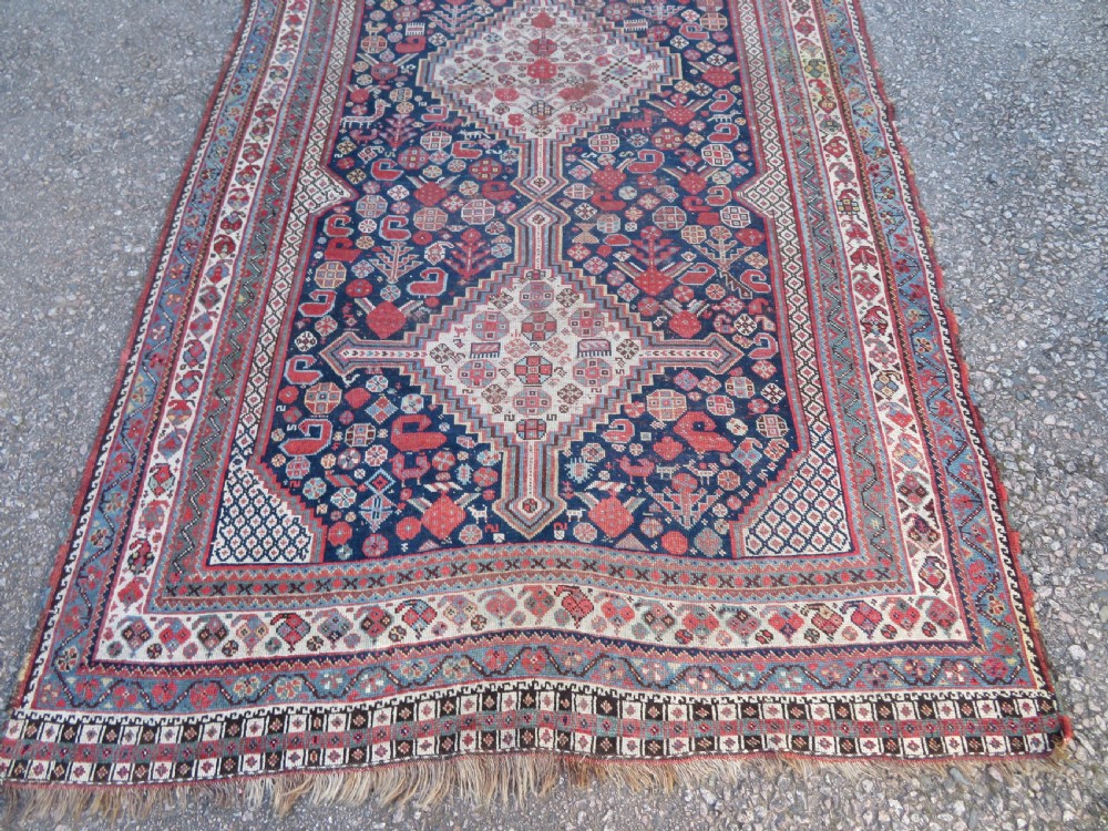 An antique hand-knotted Persian Khamseh carpet featuring three central diamond pole medallions on a dark navy blue field filled with geometric tribal bird and flower motifs surrounded by intricate decorative borders. View V