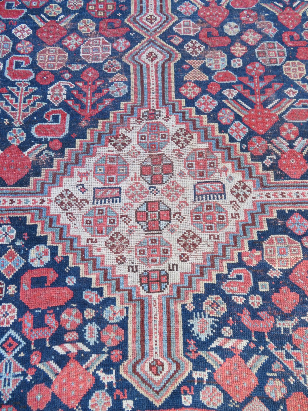 An antique hand-knotted Persian Khamseh carpet featuring three central diamond pole medallions on a dark navy blue field filled with geometric tribal bird and flower motifs surrounded by intricate decorative borders. View VI