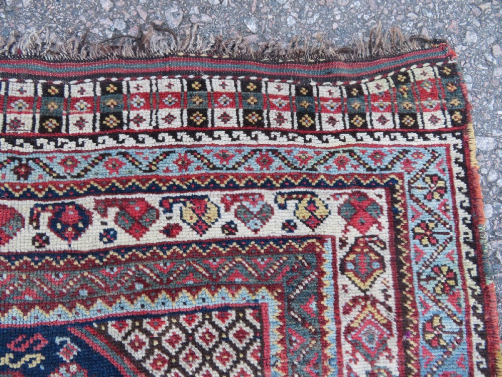 An antique hand-knotted Persian Khamseh carpet featuring three central diamond pole medallions on a dark navy blue field filled with geometric tribal bird and flower motifs surrounded by intricate decorative borders. View X
