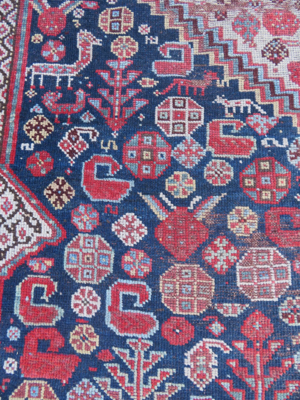 An antique hand-knotted Persian Khamseh carpet featuring three central diamond pole medallions on a dark navy blue field filled with geometric tribal bird and flower motifs surrounded by intricate decorative borders. View XV