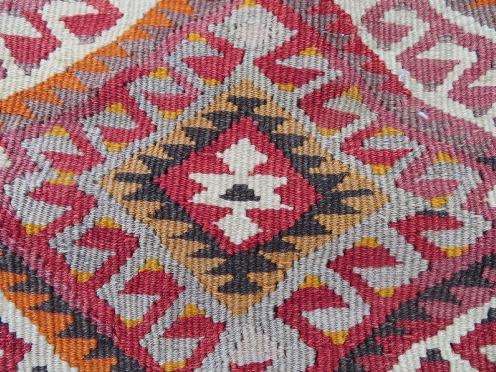 A flatwoven Anatolian kilim grain sack featuring geometric diamond motifs in red, orange, cream, and brown wool with corner tassels. View II