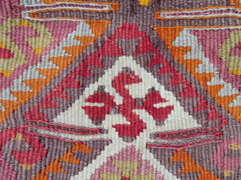 A flatwoven Anatolian kilim grain sack featuring geometric diamond motifs in red, orange, cream, and brown wool with corner tassels. View III