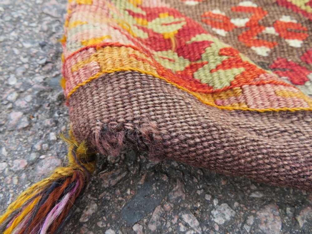 A flatwoven Anatolian kilim grain sack featuring geometric diamond motifs in red, orange, cream, and brown wool with corner tassels. View VII