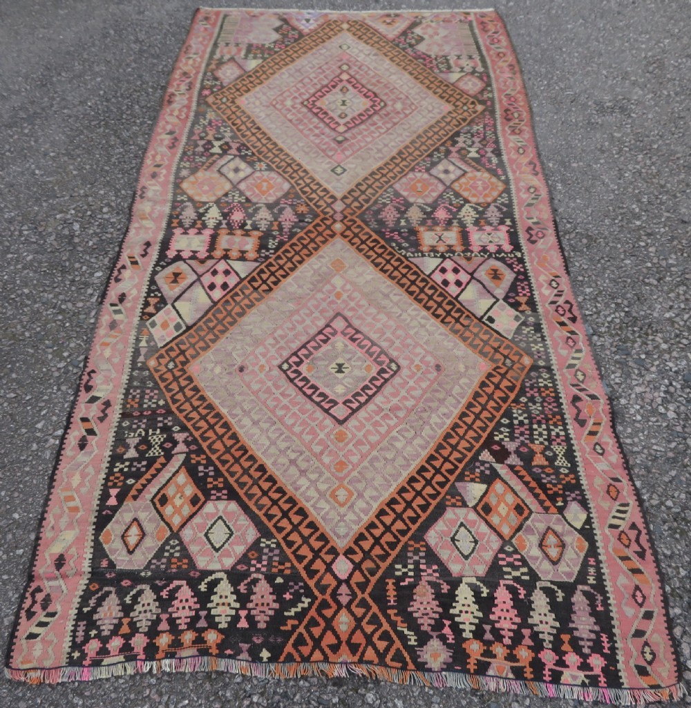 An antique flatwoven Turkish kilim rug featuring central diamond medallions and geometric borders in shades of pink, terracotta, cream, and dark brown.