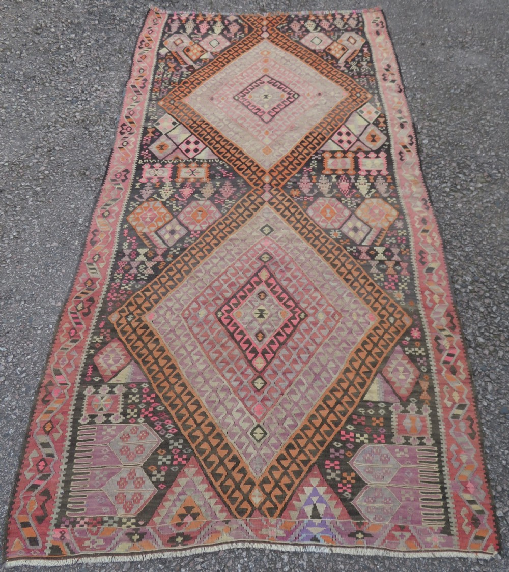 An antique flatwoven Turkish kilim rug featuring central diamond medallions and geometric borders in shades of pink, terracotta, cream, and dark brown. View II