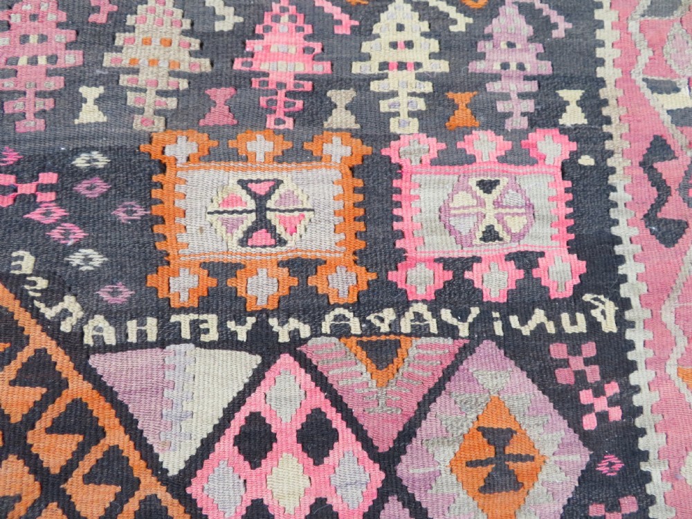 An antique flatwoven Turkish kilim rug featuring central diamond medallions and geometric borders in shades of pink, terracotta, cream, and dark brown. View III