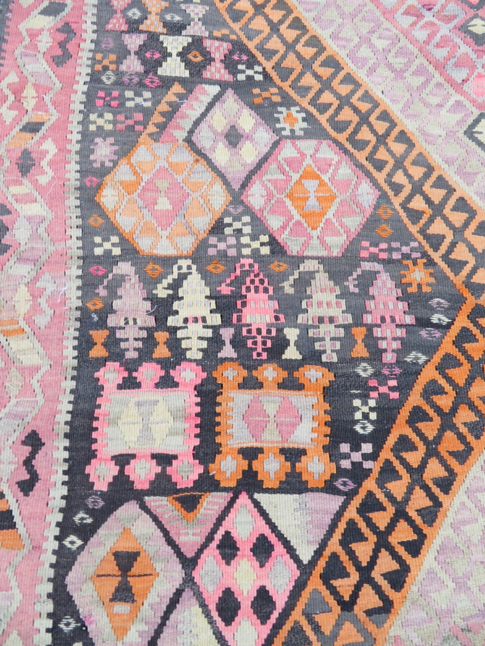 An antique flatwoven Turkish kilim rug featuring central diamond medallions and geometric borders in shades of pink, terracotta, cream, and dark brown. View V