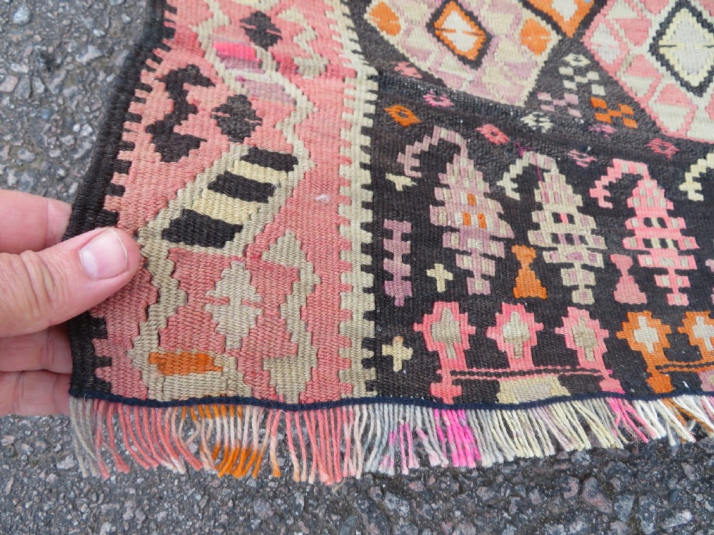 An antique flatwoven Turkish kilim rug featuring central diamond medallions and geometric borders in shades of pink, terracotta, cream, and dark brown. View VI
