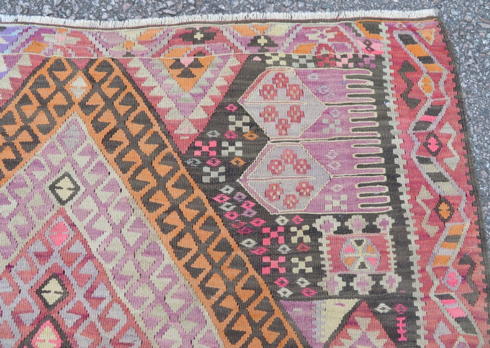 An antique flatwoven Turkish kilim rug featuring central diamond medallions and geometric borders in shades of pink, terracotta, cream, and dark brown. View IX
