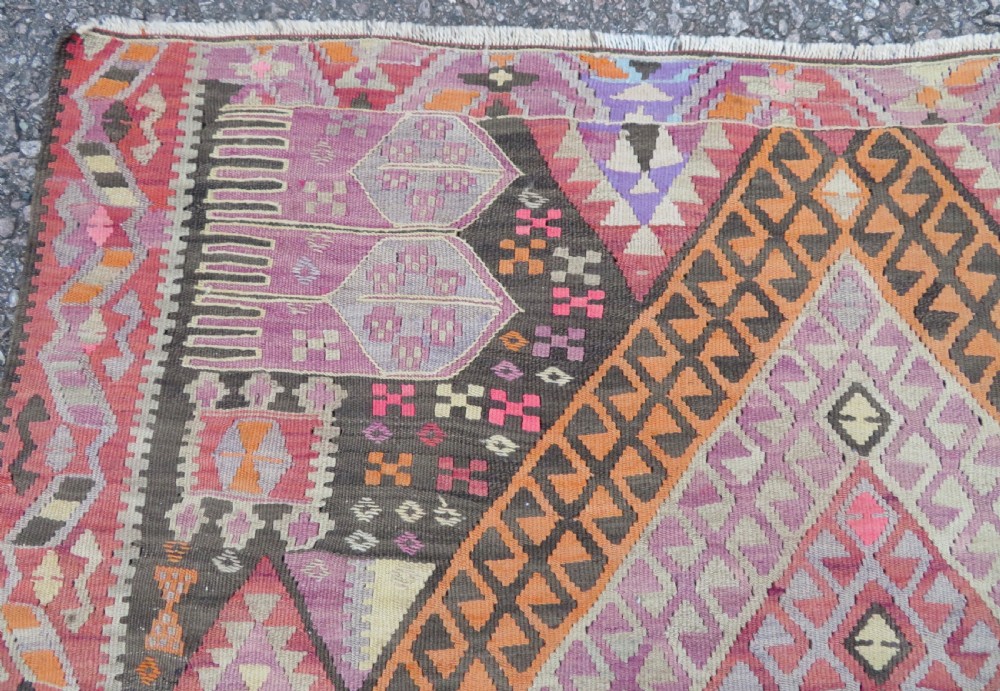 An antique flatwoven Turkish kilim rug featuring central diamond medallions and geometric borders in shades of pink, terracotta, cream, and dark brown. View X