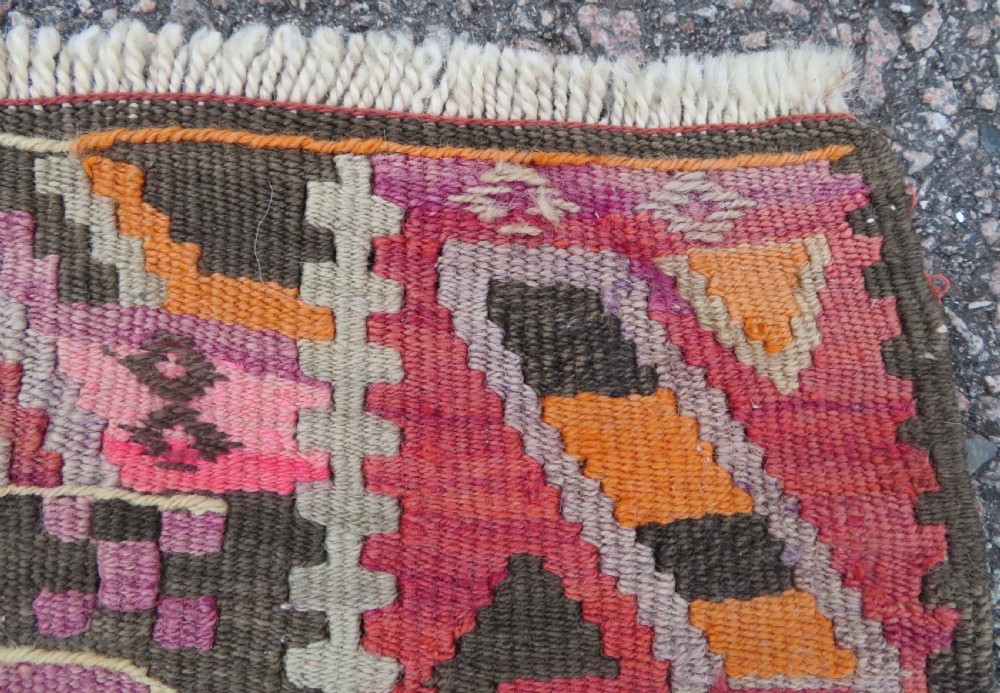 An antique flatwoven Turkish kilim rug featuring central diamond medallions and geometric borders in shades of pink, terracotta, cream, and dark brown. View XII