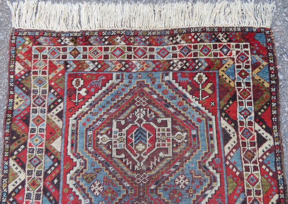 A small hand-knotted wool rug featuring three diamond geometric medallions on a blue and red field surrounded by detailed geometric borders with fringe at the ends. View III