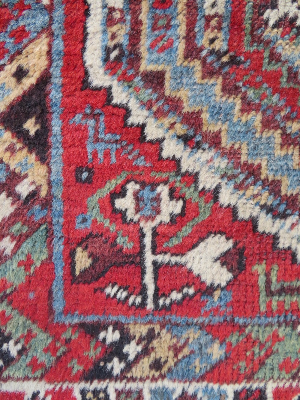 A small hand-knotted wool rug featuring three diamond geometric medallions on a blue and red field surrounded by detailed geometric borders with fringe at the ends. View VIII