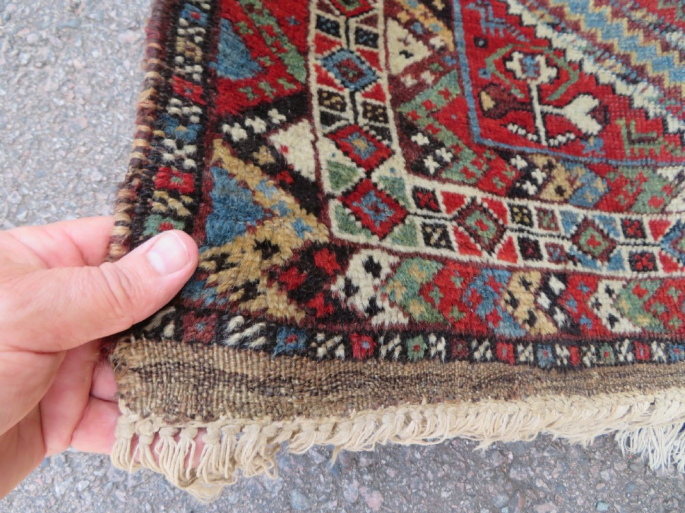 A small hand-knotted wool rug featuring three diamond geometric medallions on a blue and red field surrounded by detailed geometric borders with fringe at the ends. View IX