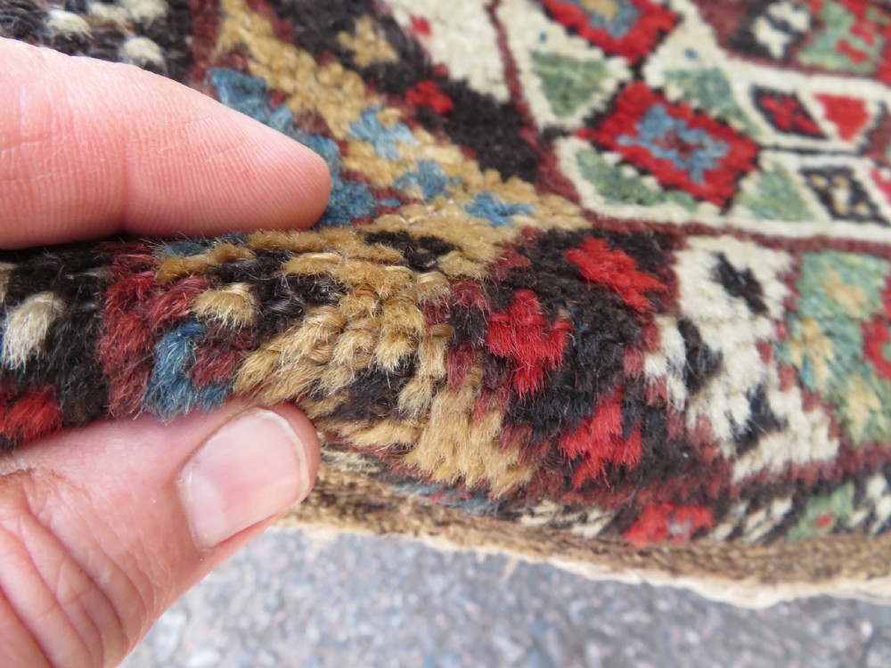 A small hand-knotted wool rug featuring three diamond geometric medallions on a blue and red field surrounded by detailed geometric borders with fringe at the ends. View X