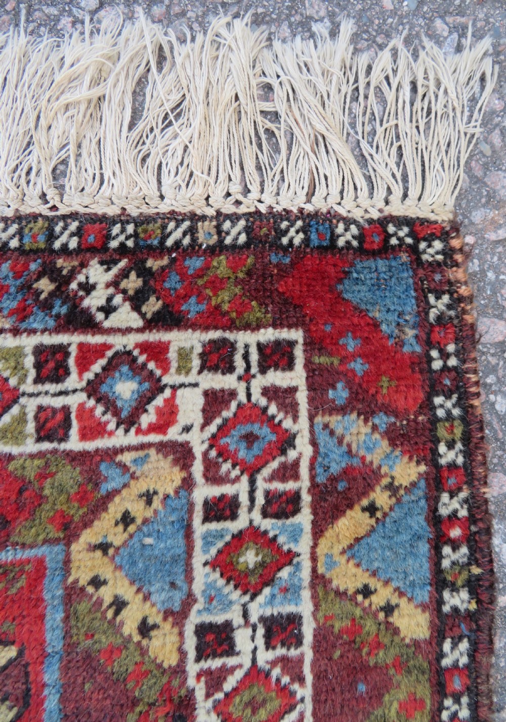 A small hand-knotted wool rug featuring three diamond geometric medallions on a blue and red field surrounded by detailed geometric borders with fringe at the ends. View XI
