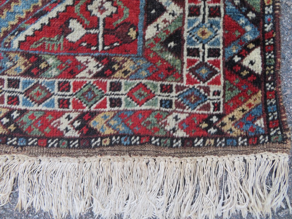 A small hand-knotted wool rug featuring three diamond geometric medallions on a blue and red field surrounded by detailed geometric borders with fringe at the ends. View XII