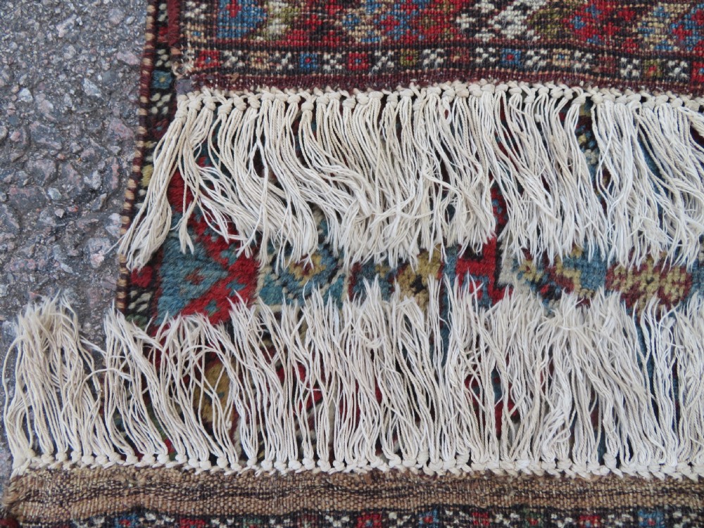 A small hand-knotted wool rug featuring three diamond geometric medallions on a blue and red field surrounded by detailed geometric borders with fringe at the ends. View XV