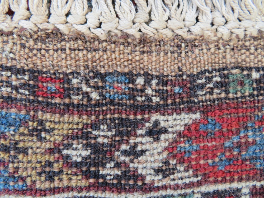 A small hand-knotted wool rug featuring three diamond geometric medallions on a blue and red field surrounded by detailed geometric borders with fringe at the ends. View XVI