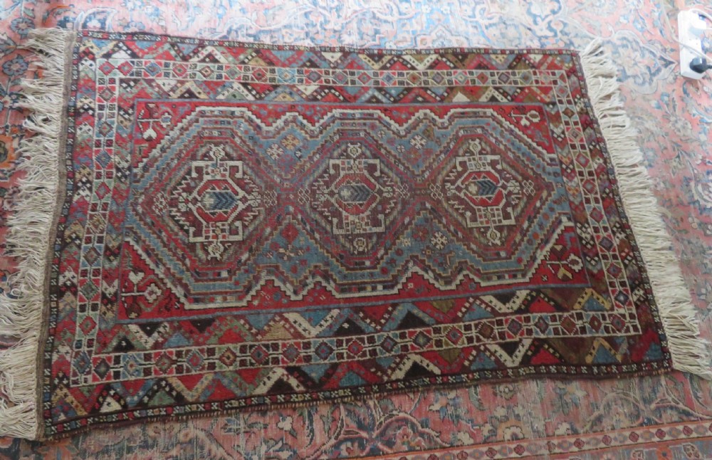 A small hand-knotted wool rug featuring three diamond geometric medallions on a blue and red field surrounded by detailed geometric borders with fringe at the ends. View XVIII