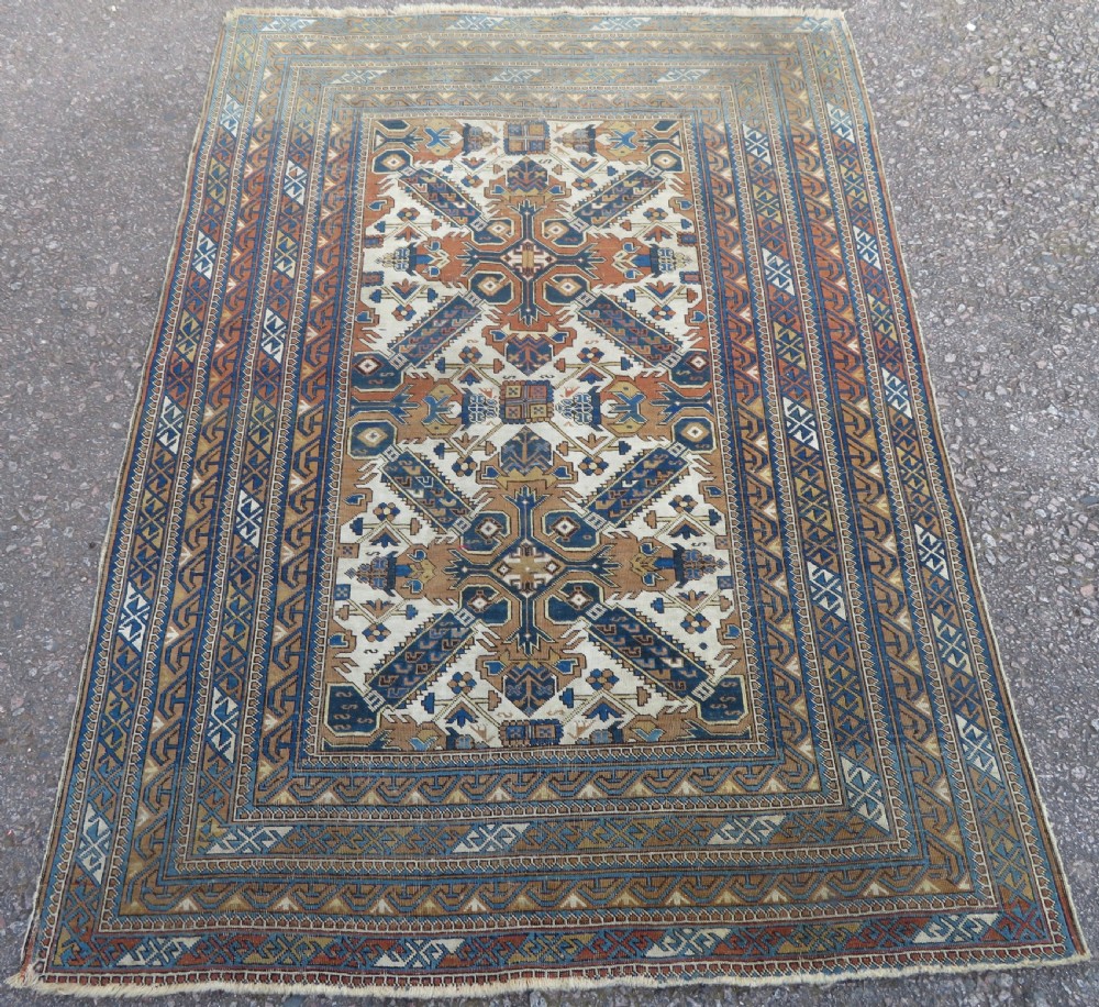 An antique hand-knotted Caucasian Kuba Seichur wool rug featuring a geometric white ground field surrounded by multi-layered patterned borders in blue, terracotta, and ochre.