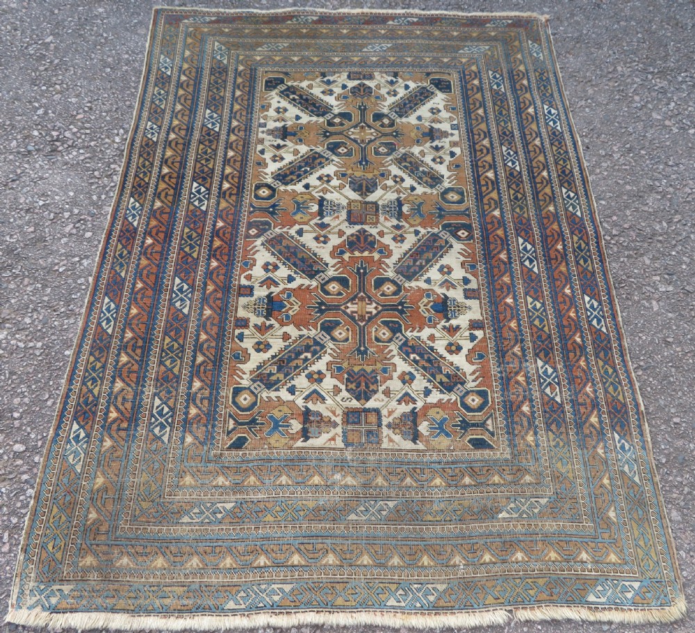 An antique hand-knotted Caucasian Kuba Seichur wool rug featuring a geometric white ground field surrounded by multi-layered patterned borders in blue, terracotta, and ochre. View II