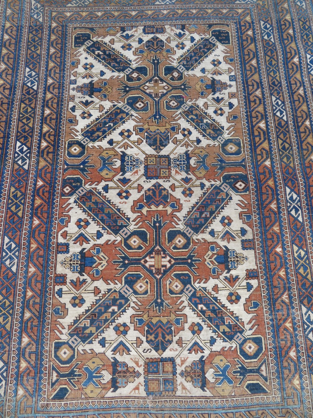 An antique hand-knotted Caucasian Kuba Seichur wool rug featuring a geometric white ground field surrounded by multi-layered patterned borders in blue, terracotta, and ochre. View III