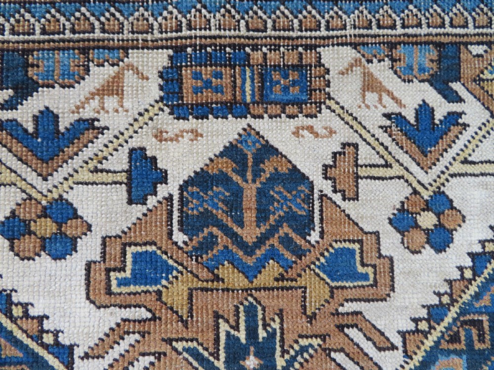 An antique hand-knotted Caucasian Kuba Seichur wool rug featuring a geometric white ground field surrounded by multi-layered patterned borders in blue, terracotta, and ochre. View IV