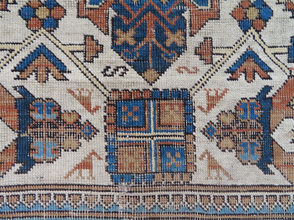 An antique hand-knotted Caucasian Kuba Seichur wool rug featuring a geometric white ground field surrounded by multi-layered patterned borders in blue, terracotta, and ochre. View VI